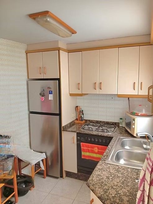 Cocina pequeña con armarios beige, nevera de acero inoxidable, cocina de gas, fregadero y encimera de granito.