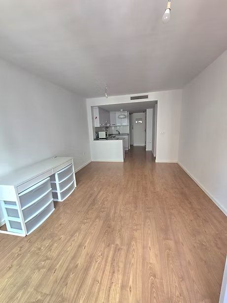 Habitación estrecha y vacía con suelo de madera y una pequeña zona de cocina al fondo.