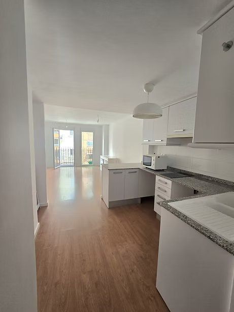 Cocina luminosa y diáfana con armarios blancos, encimeras de granito y suelos de madera
