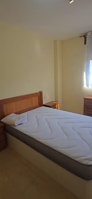 Habitación pequeña con cama individual, cabecero de madera y ventana con cortinas.