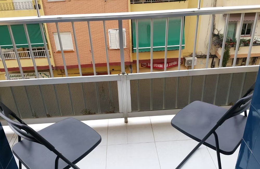 Dos sillas plegables negras en un balcón con vistas a un patio interior con ventanas de apartamentos.