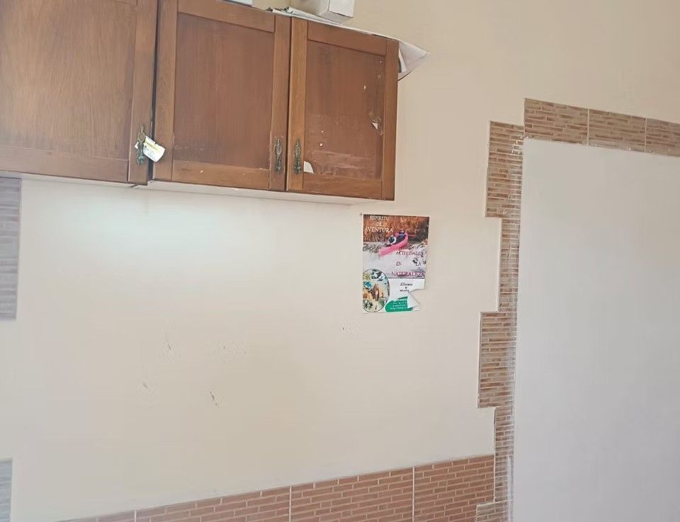 Pared con armarios de madera sobre un salpicadero de azulejos y un pequeño póster, probablemente en una cocina o lavadero.