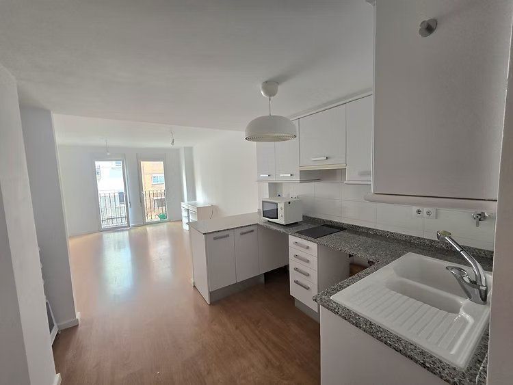Cocina y sala de estar modernas, luminosas y vacías, con gabinetes blancos, encimeras grises y pisos de madera.