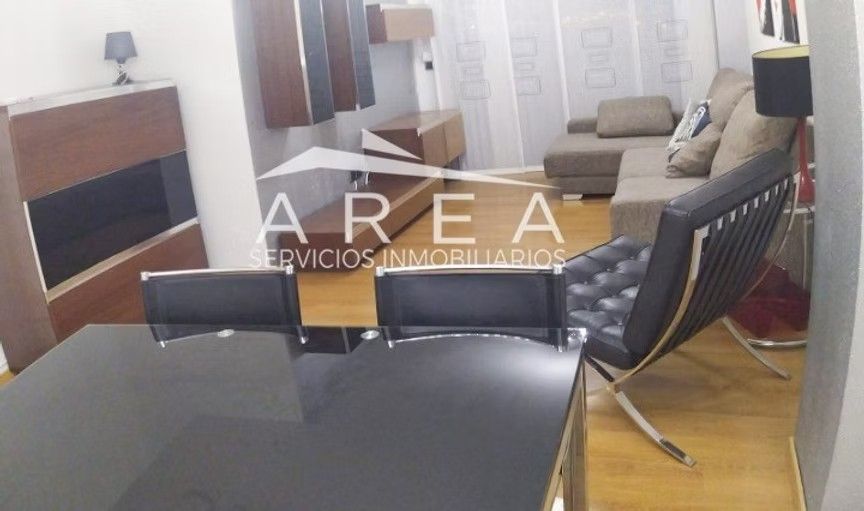 Sala de estar con sillas negras, sofá gris, mueble para TV y grandes ventanales con cortinas transparentes.