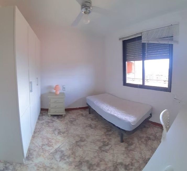 Habitación pequeña con cama individual, armario blanco, mesita de noche y ventana con persianas.