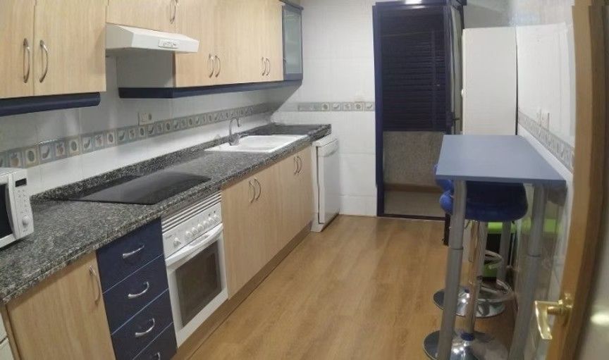 Cocina vacía con armarios de madera clara, encimeras moteadas, estufa y una estrecha barra de desayuno junto a una puerta.