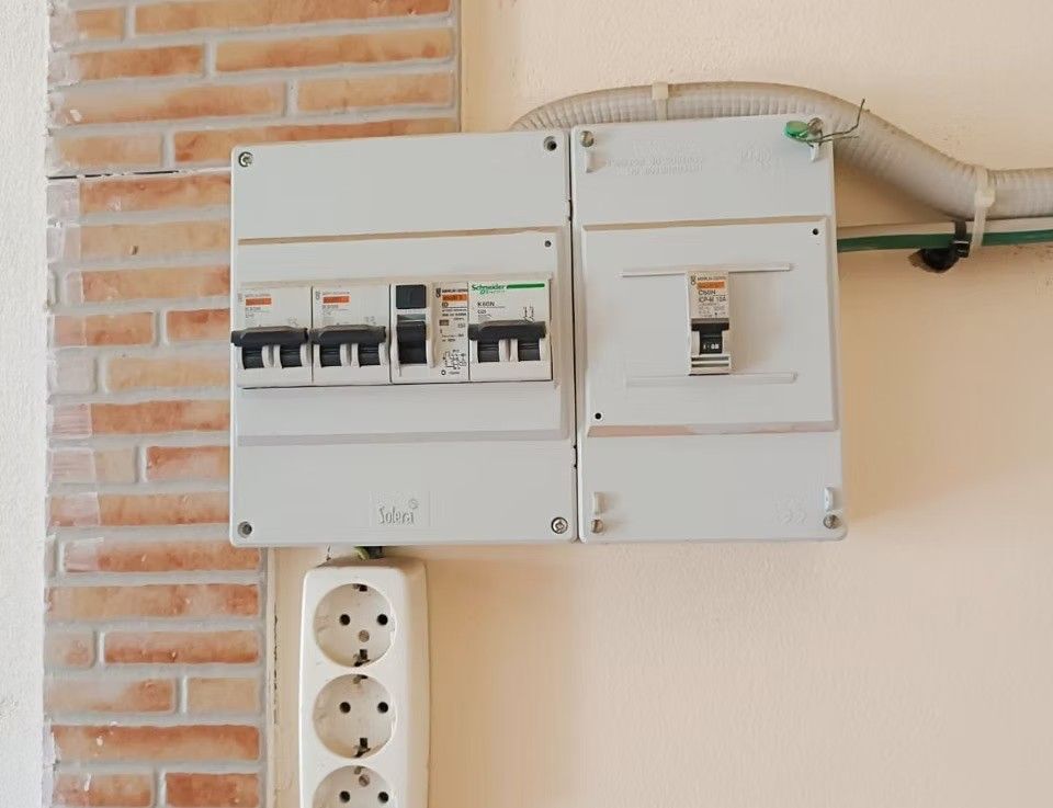 Paneles de interruptores eléctricos blancos montados en una pared de ladrillo encima de una regleta de tomas de corriente.