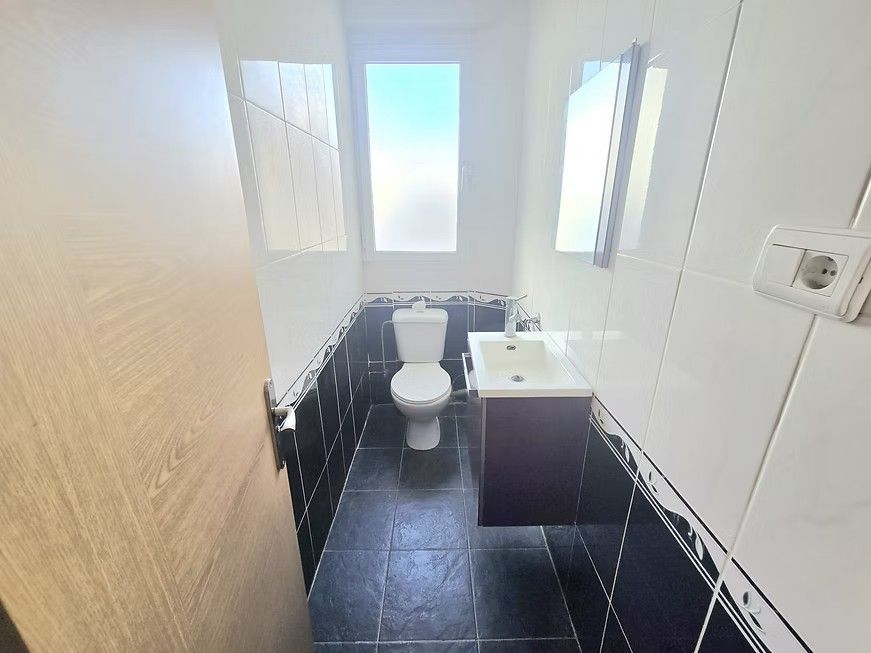 Baño pequeño con azulejos blancos y negros, inodoro, lavabo y luz de ventana.