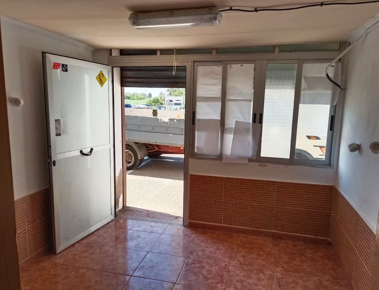 Habitación vacía con suelo de baldosas, puerta abierta y ventanas correderas con vistas a un camión aparcado en el exterior.
