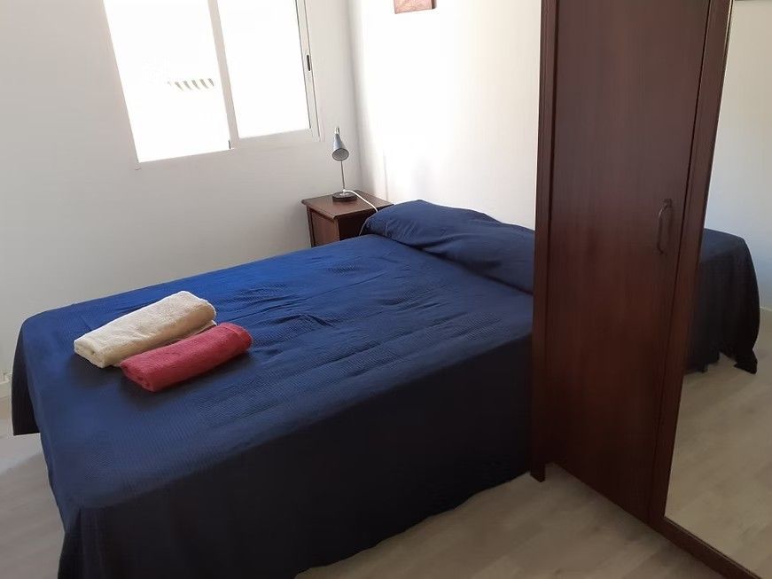 Habitación pequeña con una colcha azul, dos toallas dobladas y un armario de madera junto a la cama.