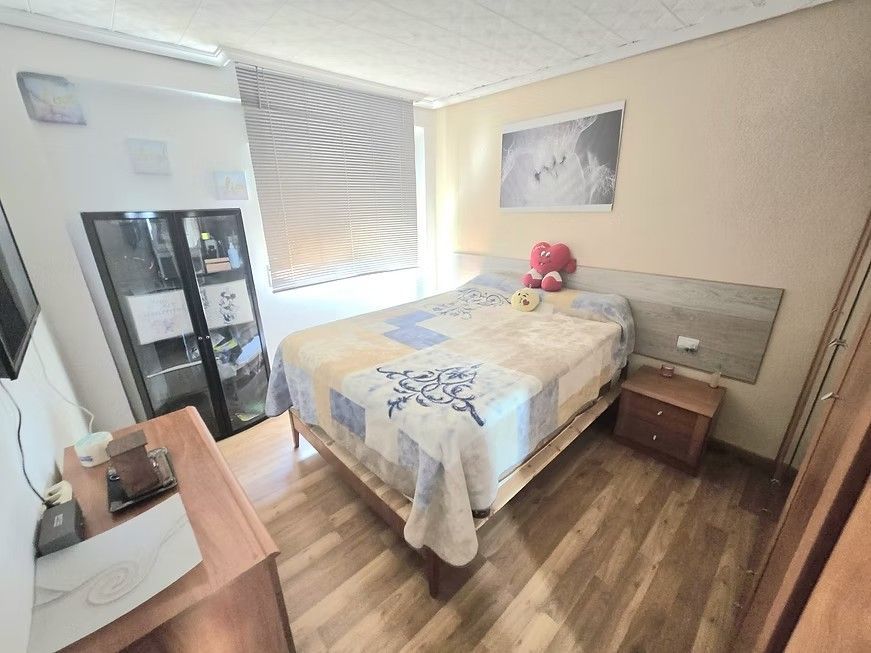 Habitación pequeña con cama, cómoda, mesita de noche, espejo, persianas y cuadros en la pared.
