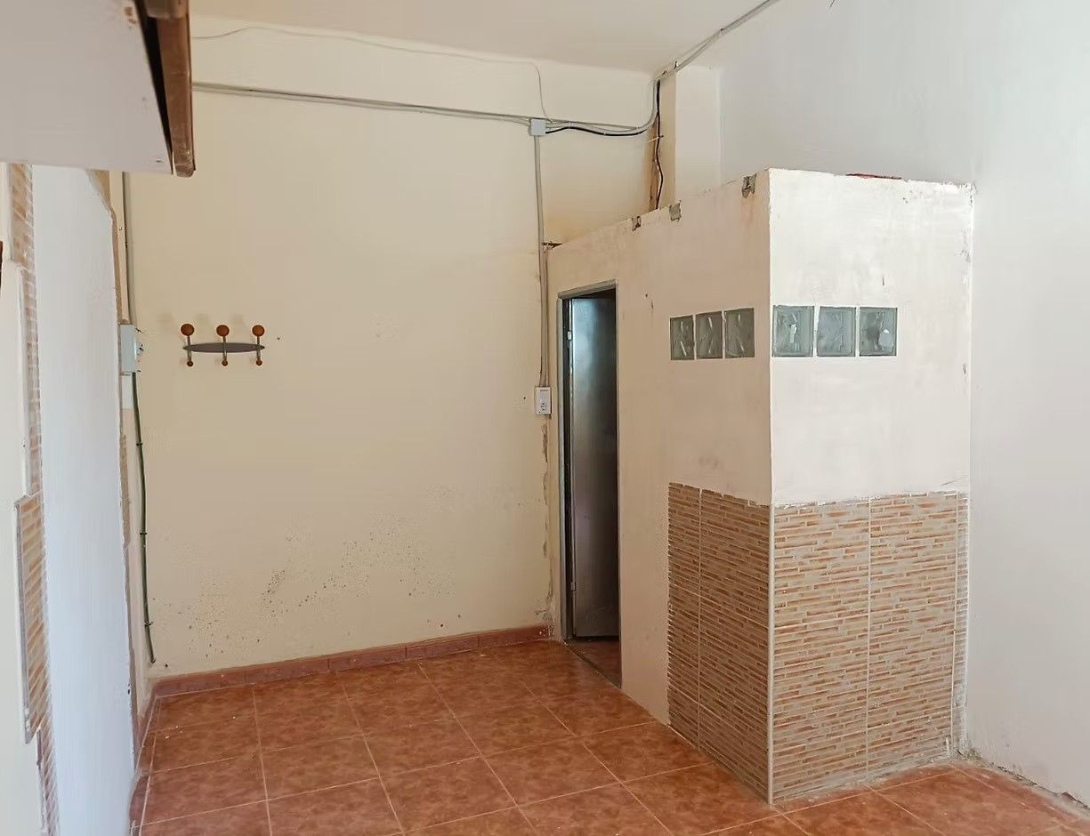 Habitación vacía con azulejos, paredes color crema, una puerta y una pequeña alcoba separada por una mampara.