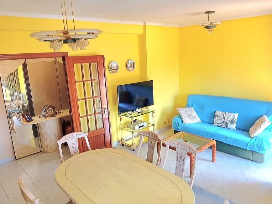 Sala de estar de color amarillo brillante con sofá azul, televisor, mesa de comedor y puerta abierta a la cocina.
