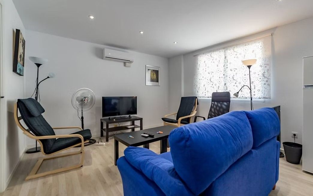 Sala de estar moderna con sofá azul, televisor, sillas negras, mesa de centro, lámpara de pie y ventanal grande.