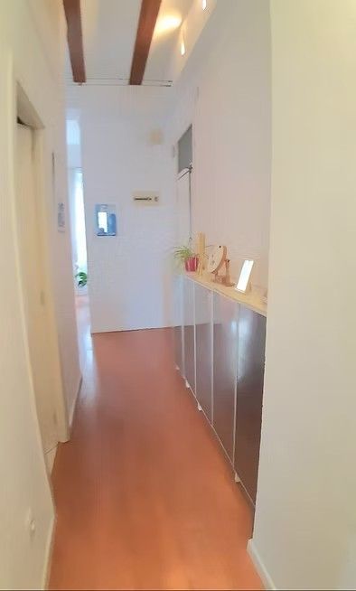 Pasillo estrecho con suelo de madera, paredes blancas, vigas en el techo y armarios a lo largo del lado derecho.