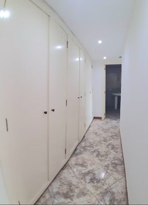 Pasillo luminoso con puertas de armario blancas, suelo de baldosas y luces empotradas en el techo que conduce a una puerta.