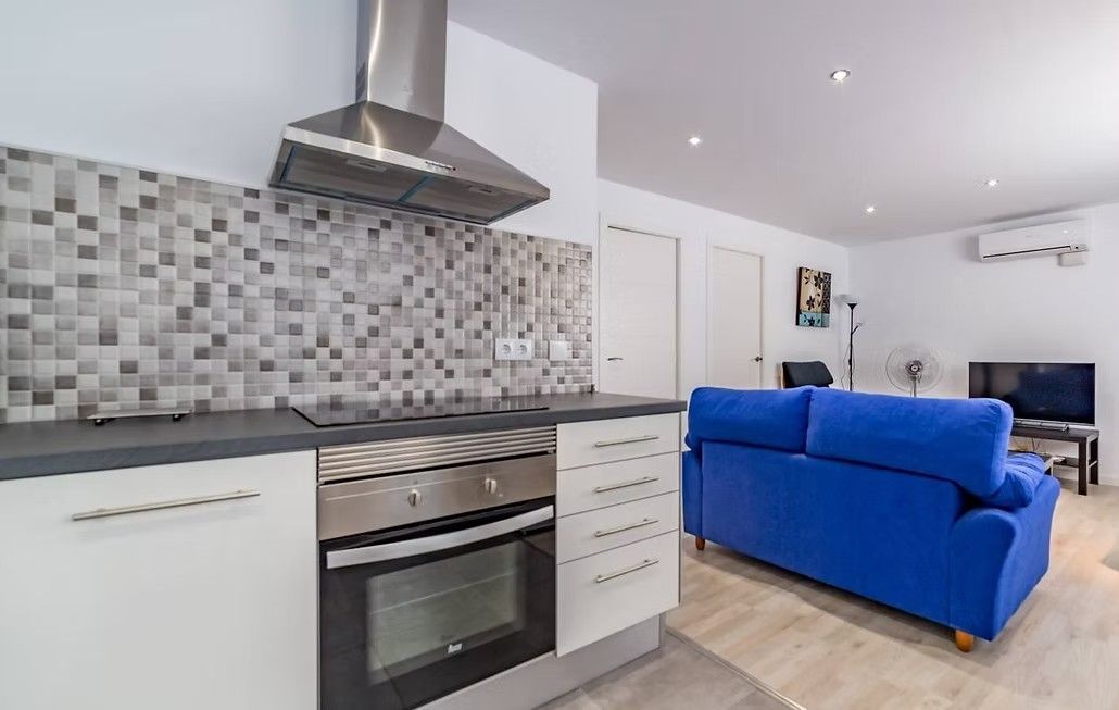 Cocina moderna con salpicadero de mosaico y horno de acero inoxidable junto a una sala de estar con un sofá azul brillante.