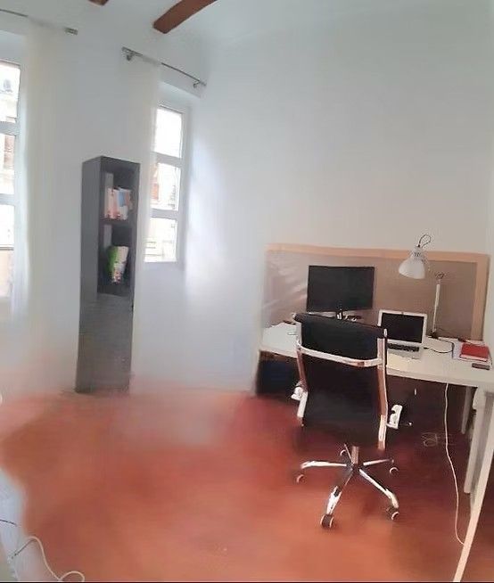 Pequeña oficina con escritorio, ordenador, silla y un armario alto gris sobre una pared blanca y suelo de madera.