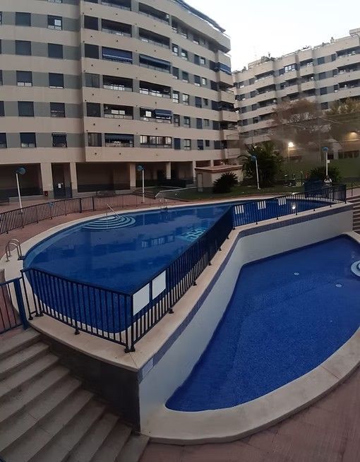 Patio del apartamento con piscina azul vacía y edificios circundantes al anochecer.