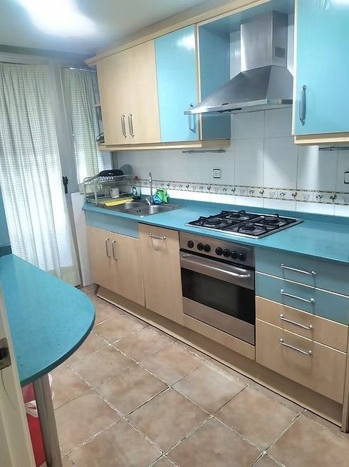 Pequeña cocina moderna con armarios azules y de madera, cocina de gas, horno y suelo de baldosas.