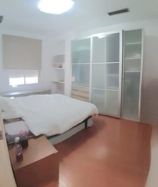 Habitación luminosa con cama blanca, puertas correderas en el armario, persianas y suelo de madera.