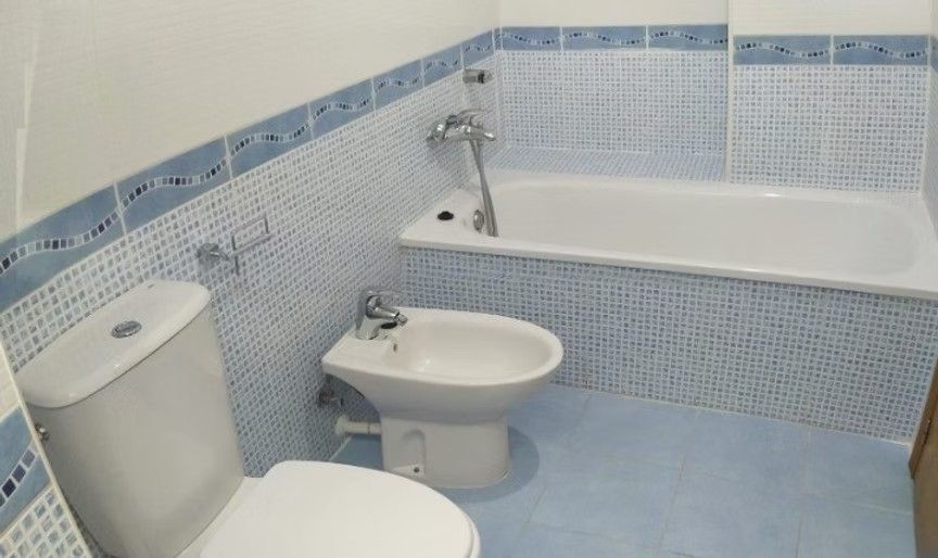 Baño pequeño con azulejos azules, inodoro, bidé, lavabo y bañera con barra de ducha.