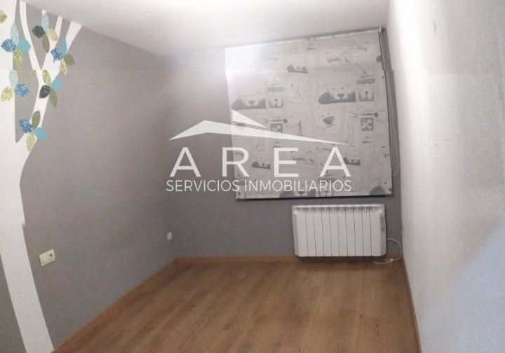 Habitación pequeña y vacía con paredes grises, suelo de madera, ventana y radiador blanco.
