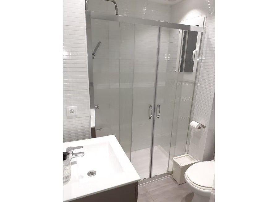 Baño moderno con cabina de ducha de cristal, lavabo blanco e inodoro.