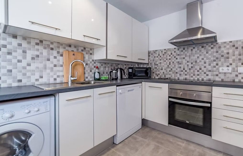 Cocina moderna blanca con salpicadero de mosaico gris, encimeras negras y electrodomésticos de acero inoxidable.
