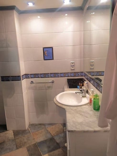 Baño pequeño con azulejos, lavabo de mármol, espejo de pared, toallero y cortina de ducha.