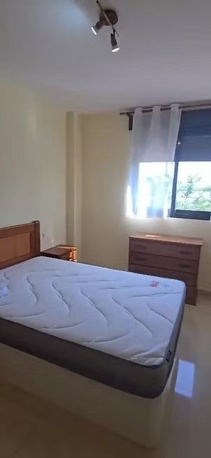 Habitación pequeña con cama, ventana y cómoda en luz tenue.