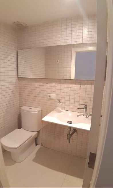 Baño pequeño con azulejos, inodoro, lavabo, armario con espejo y puerta de ducha.