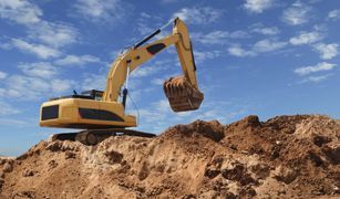 Una excavadora amarilla está sentada encima de una pila de tierra.