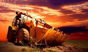 Una excavadora está sentada sobre un campo de tierra al atardecer.
