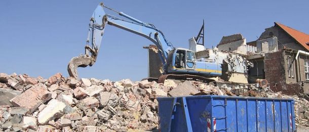 Una excavadora azul está demoliendo un edificio al lado de un contenedor de basura azul.