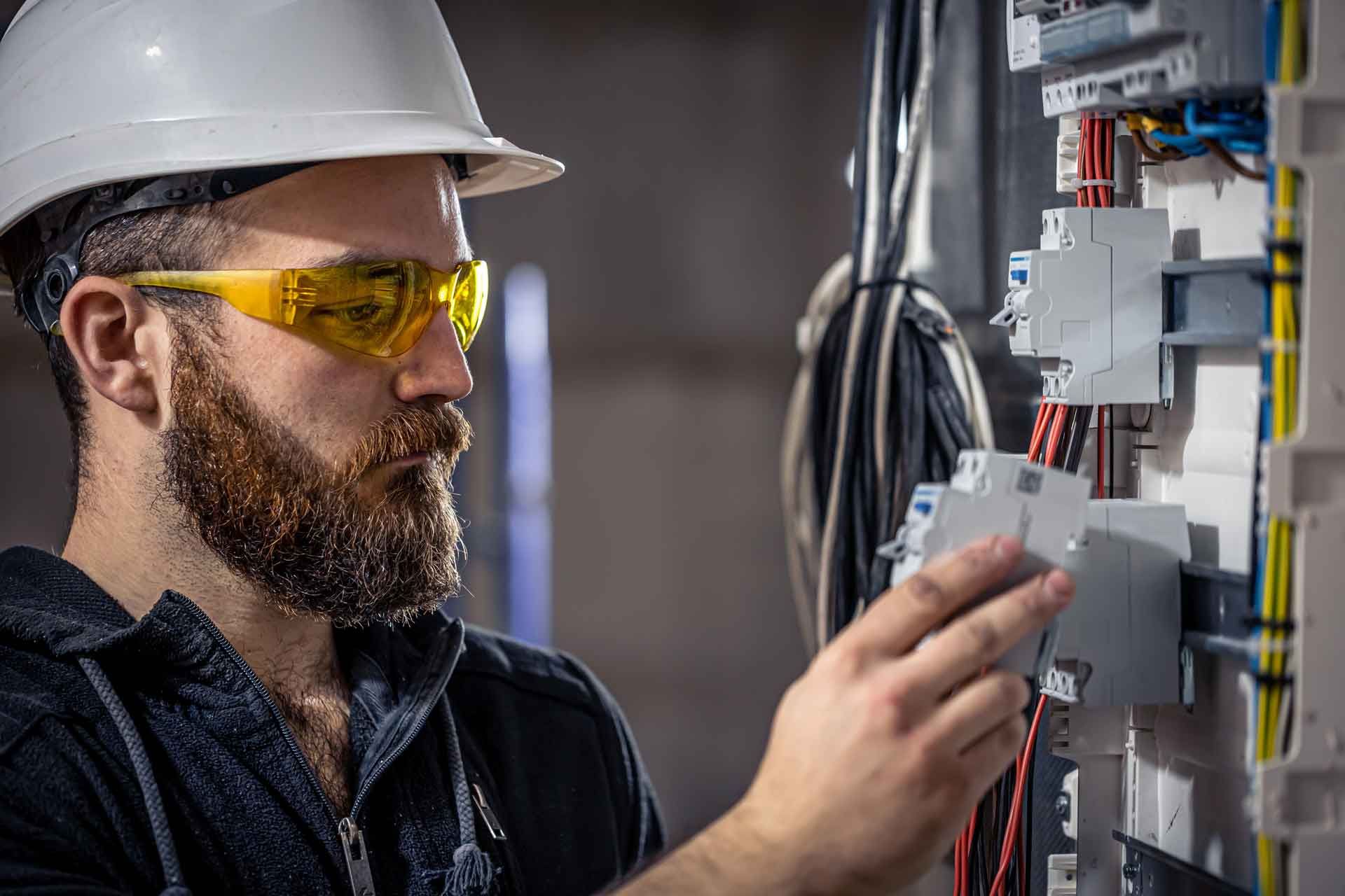 Un electricista que lleva casco y gafas de seguridad está trabajando en una caja eléctrica.