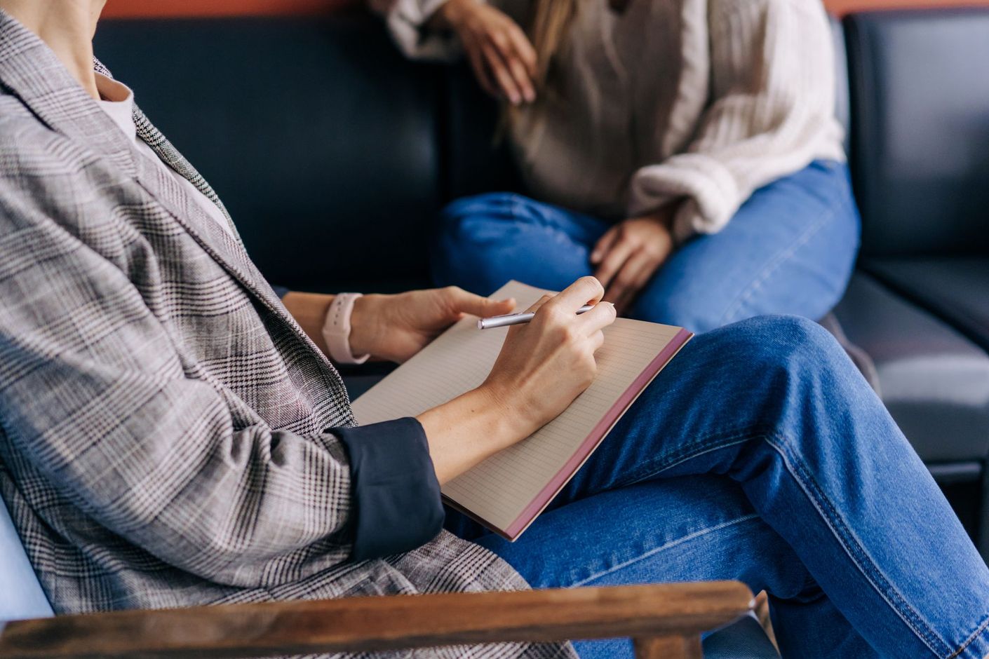 Une personne prend des notes pendant une consultation ; une autre personne est assise sur un canapé à proximité.