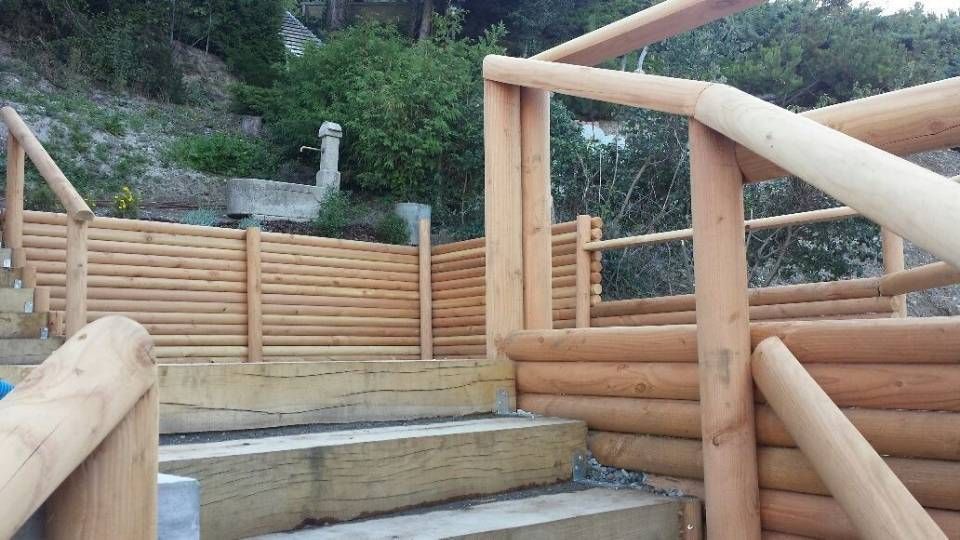 Escalier extérieur en bois et rambarde le long d'une allée en terrasses, avec une clôture et de la verdure au-delà.