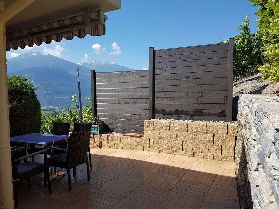 Terrasse avec table à manger extérieure, mur en pierre et vue sur la montagne sous un ciel ensoleillé