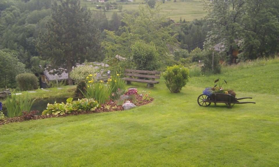 Jardin verdoyant et luxuriant avec parterres de fleurs, arbres, bancs et une brouette sur la pelouse