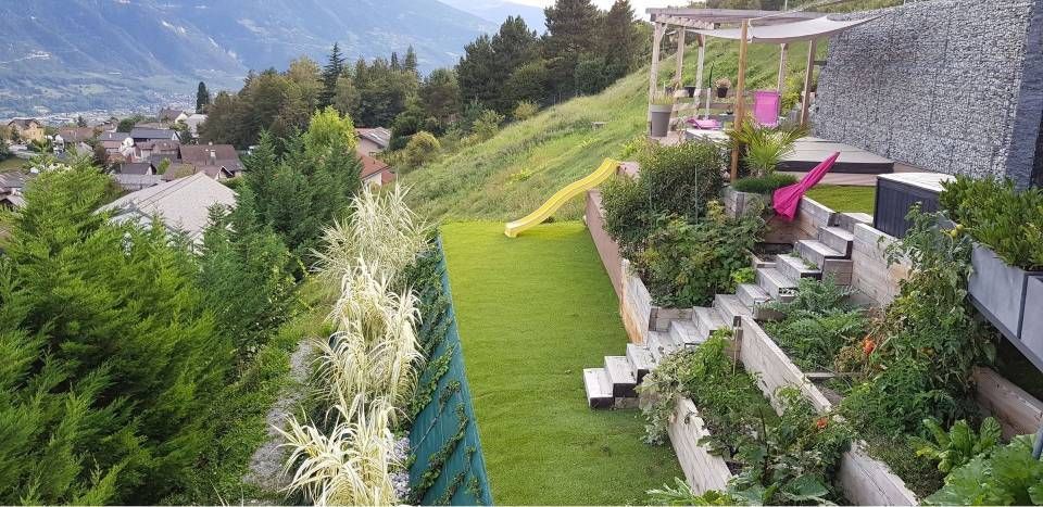 Jardin en terrasses avec pelouse verte, plantes fleuries, chaises longues et vue sur la montagne