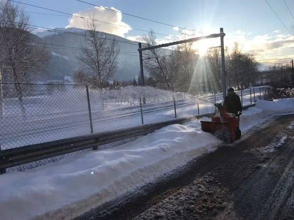 Personne déneigeant le bord d'une route près d'une clôture enneigée au lever du soleil