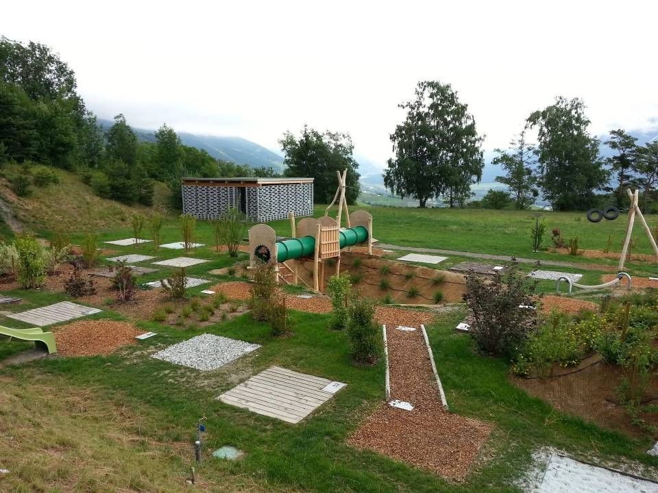 Jardin paysager avec pas japonais, parterres surélevés et un banc vert dans un parc gazonné