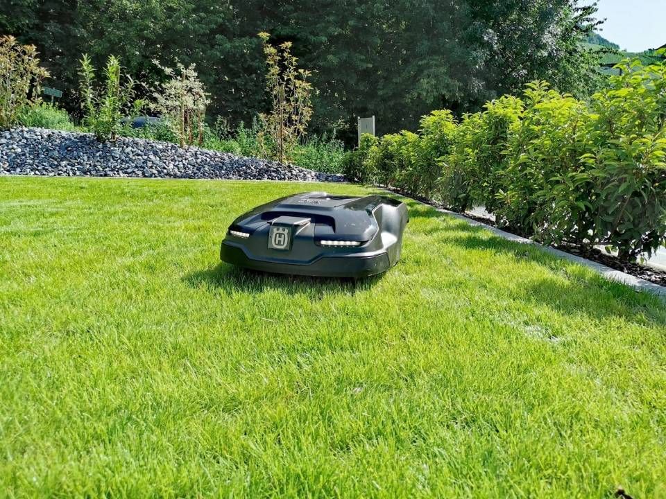 Voiture de sport noire garée sur une pelouse, près d'un muret en pierre et d'arbres.