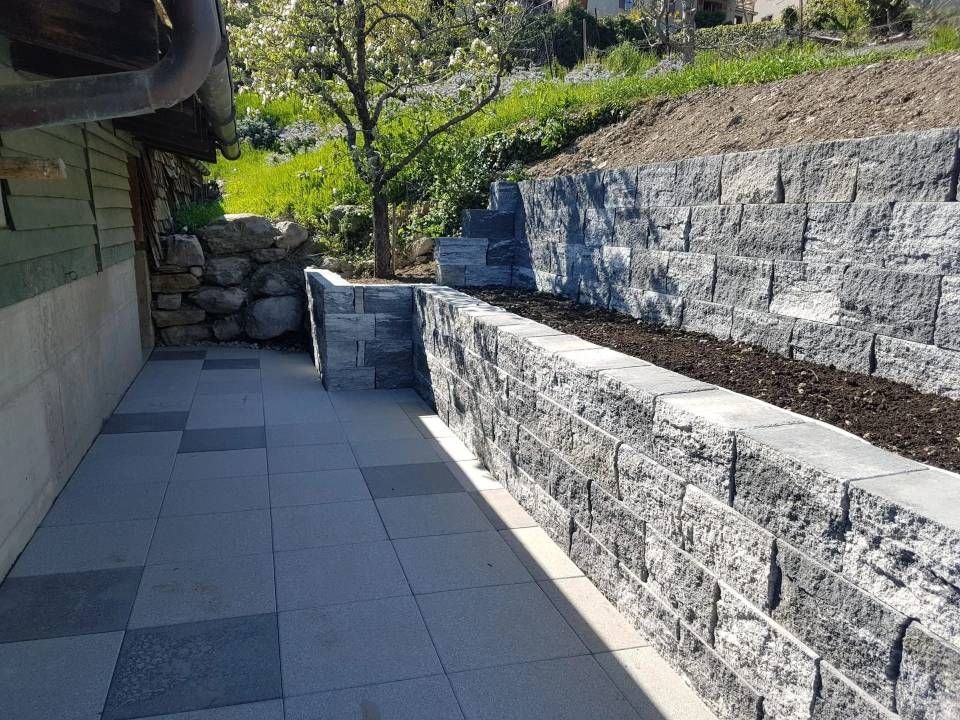 Étroite allée pavée longeant des murs de soutènement en pierre et des parterres de jardin par une journée ensoleillée