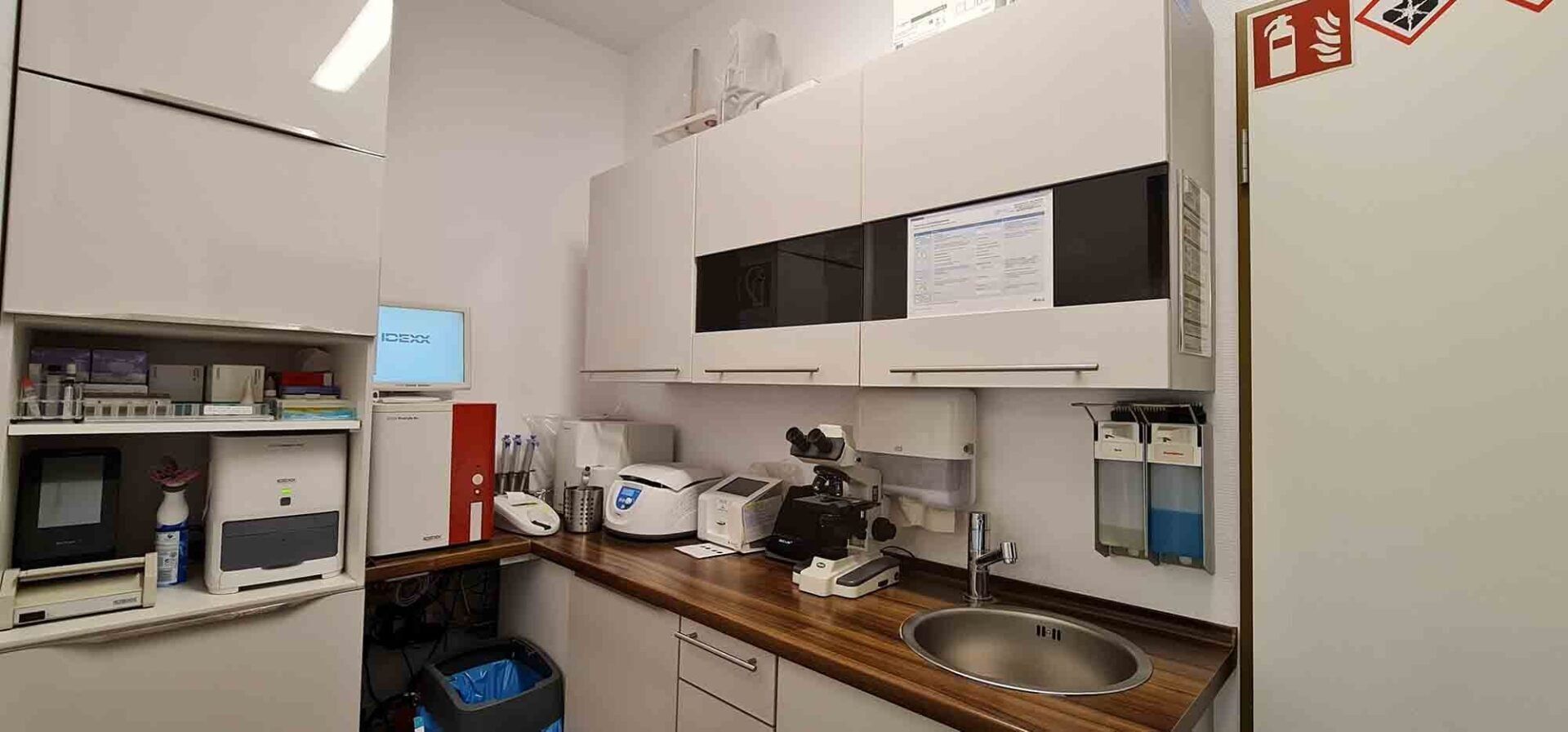 Eine Küche mit weißen Schränken, einer Spüle, einem Kühlschrank und einem Mikroskop.