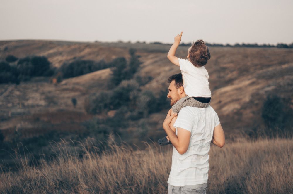 Un hombre lleva un niño sobre sus hombros en un campo.