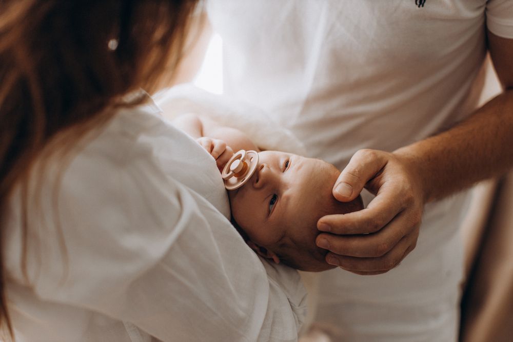 Una mujer sostiene a un bebé recién nacido con un chupete en la boca.
