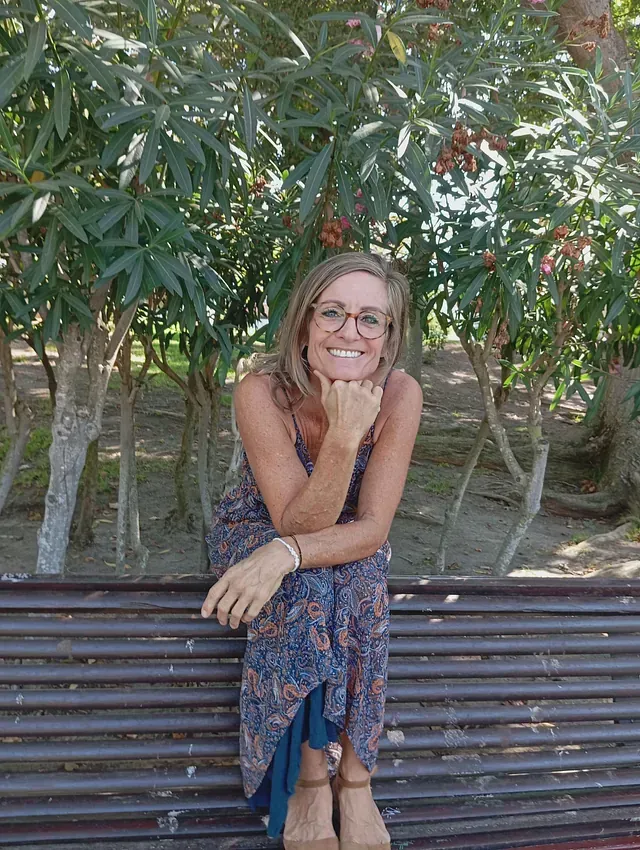 Una mujer está sentada en un banco del parque con la mano en la barbilla.