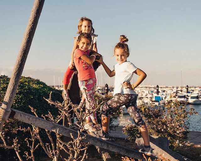 Tres niñas están paradas sobre una viga de madera tomadas de la mano.